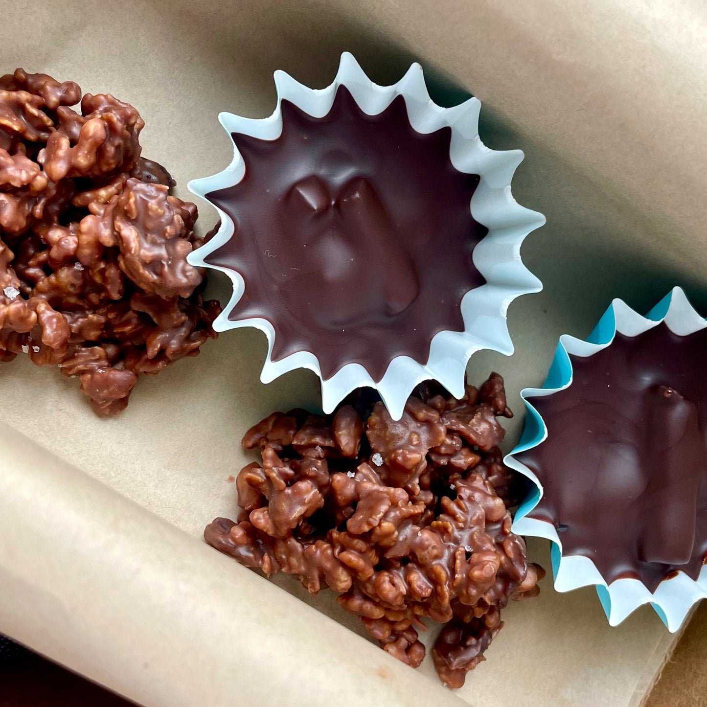 Overhead view of 2 hazelnut and orange chocolate cups and 2 rochers in a kraft box.