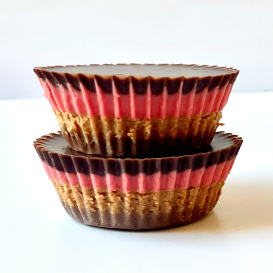 Two chocolate-covered peanut butter cups with layers of pink stacked on a white background