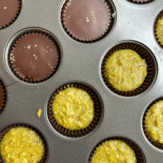 View from overhead of crunch cups being completed, some with dark chocolate layer and sprinkle of salt, some with the pistachio praline and toasted filo base.