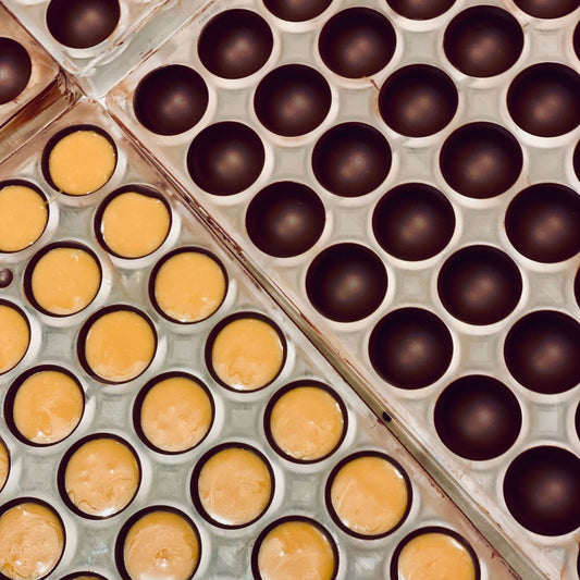 Overhead view of open chocolate domes, some empty, some filled with salted caramel. All still inside of the polycarbonate molds.