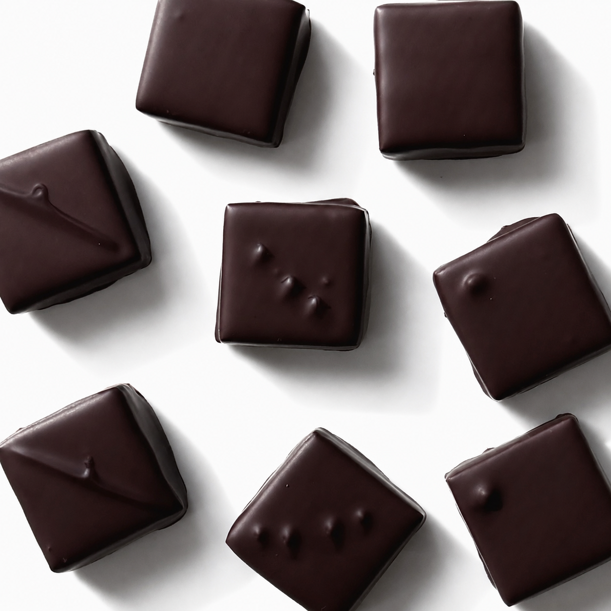 Nine square dark chocolate pieces with glossy chocolate drizzle, arranged on a clean white background.