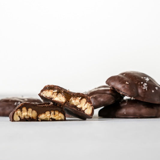 pile of dark chocolate covered pecan clusters, cut in half with pecans and caramel are showing.