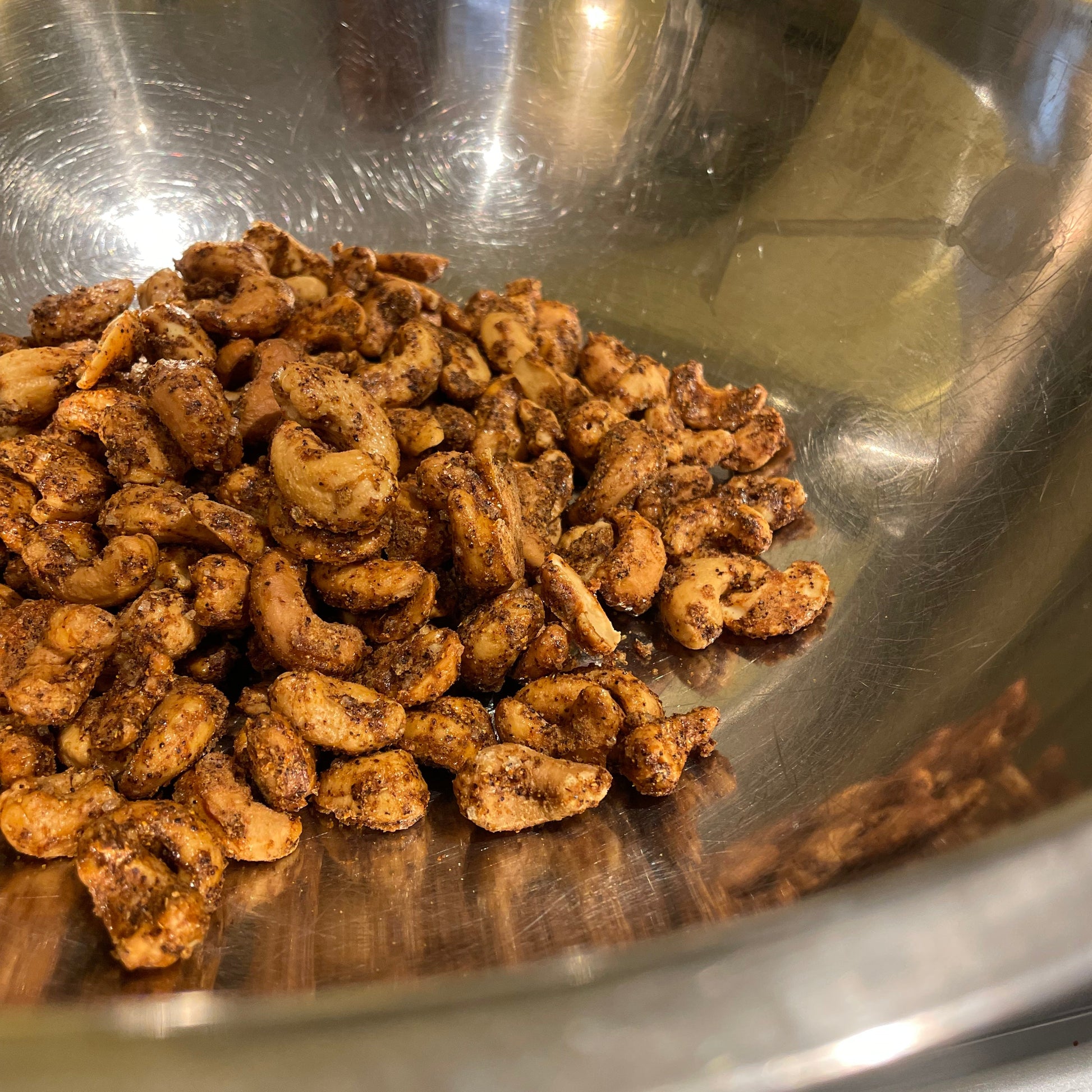 Metal bowl filled with seasoned cashews on a reflective surface