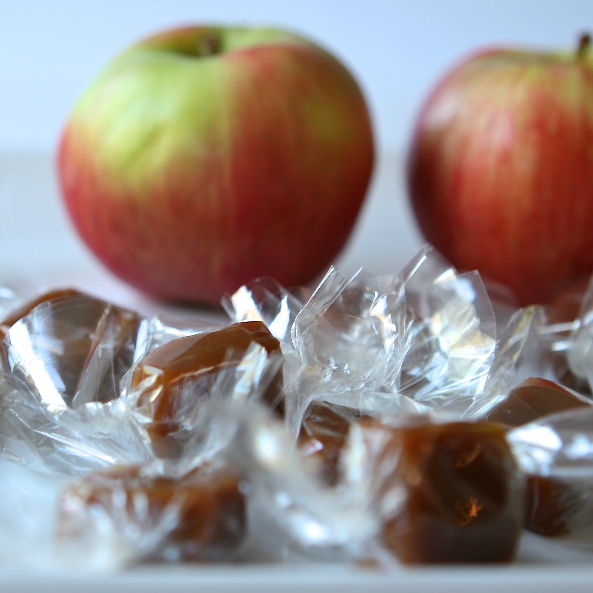 Caramels wrapped in cellophane with two apples in the background