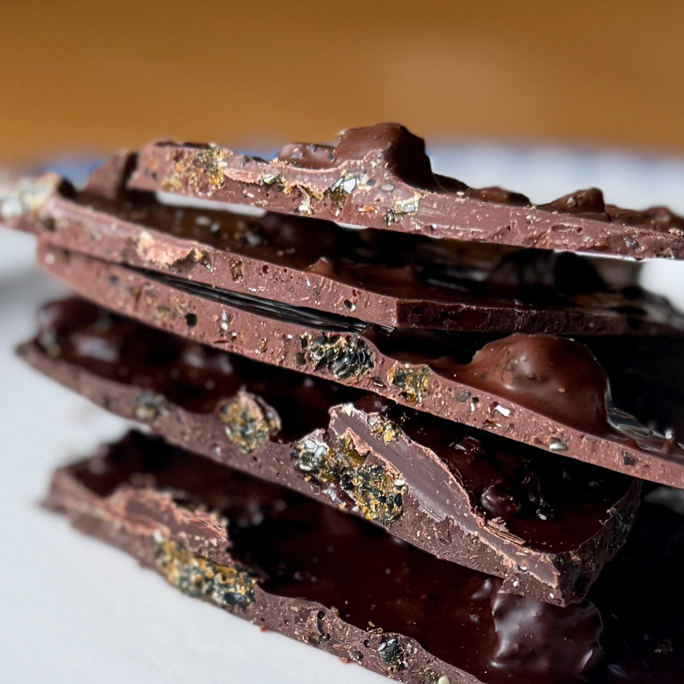 Stack of dark chocolate with visible nuts and sea salt on a white surface.