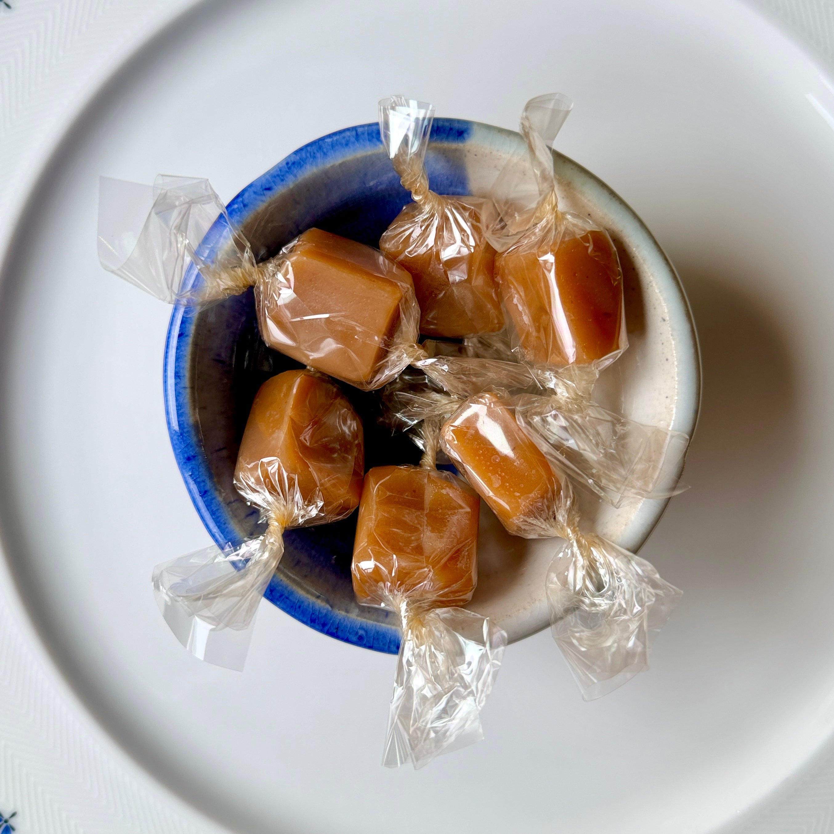 Caramel candies in clear wrappers inside a blue and white container on a white plate.