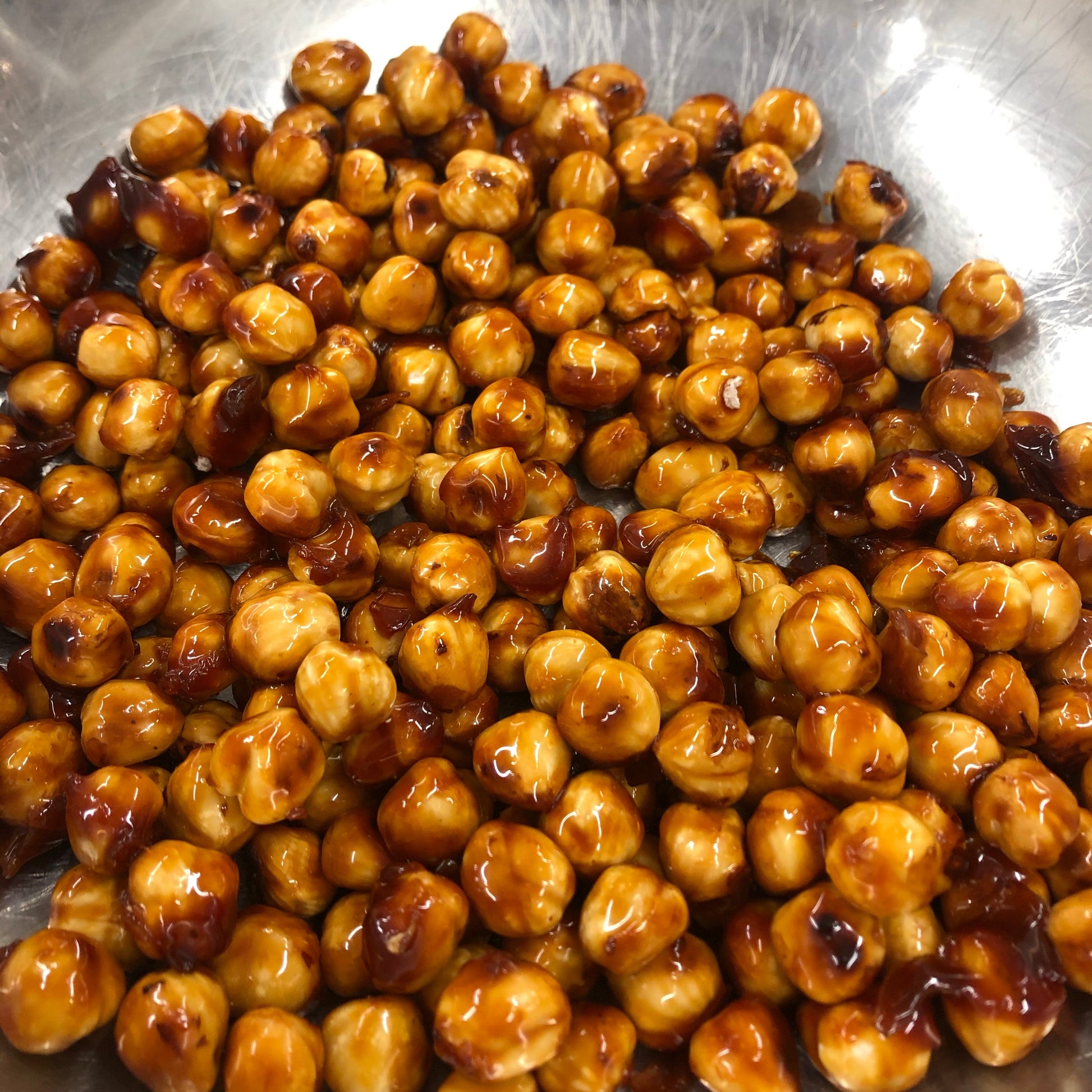 Bowl of roasted chickpeas with a glossy coating on a metal surface