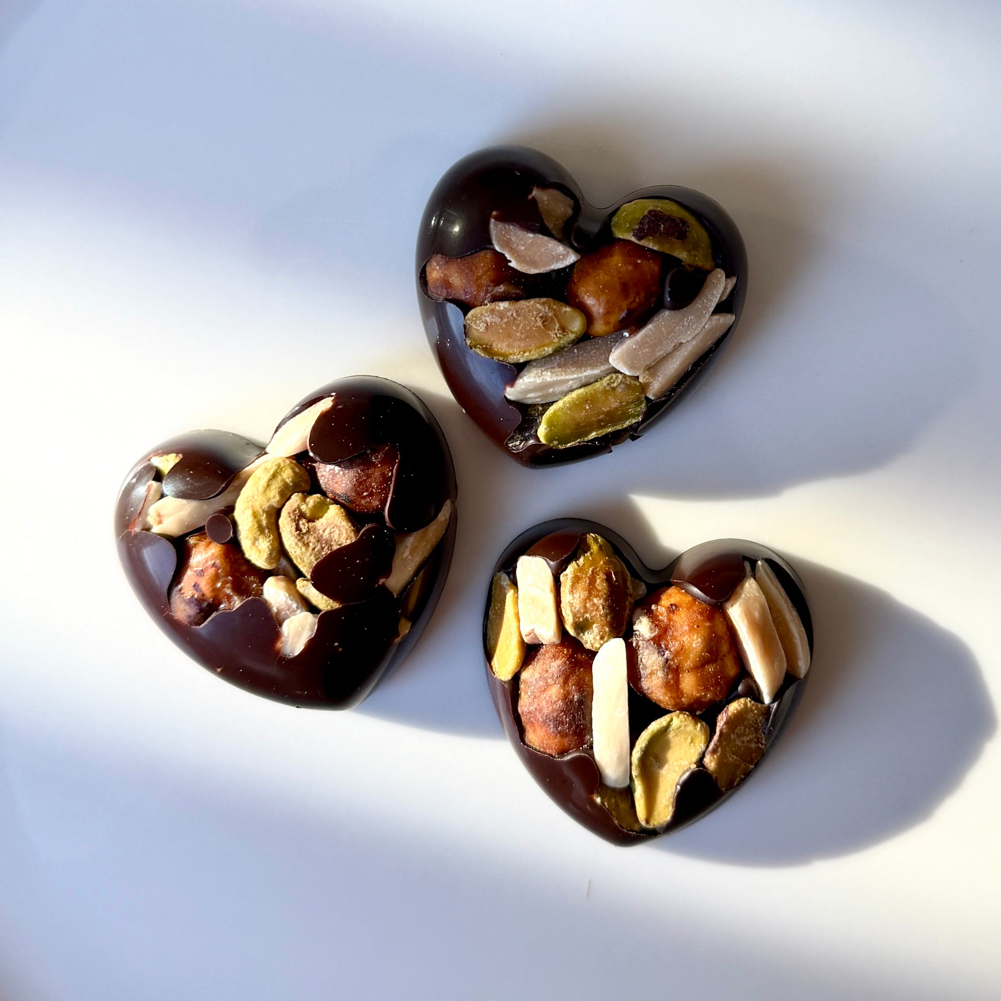 Three heart-shaped chocolate truffles with nuts on a white background
