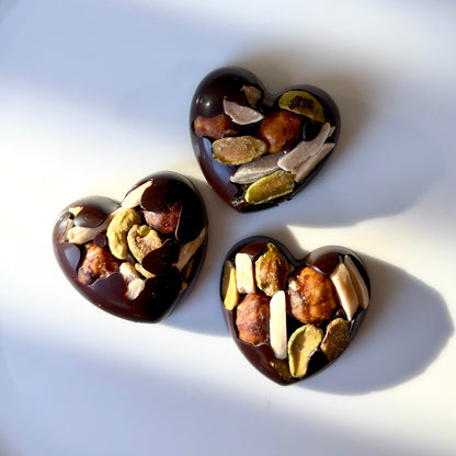 Three heart-shaped chocolate truffles with nuts on a white background
