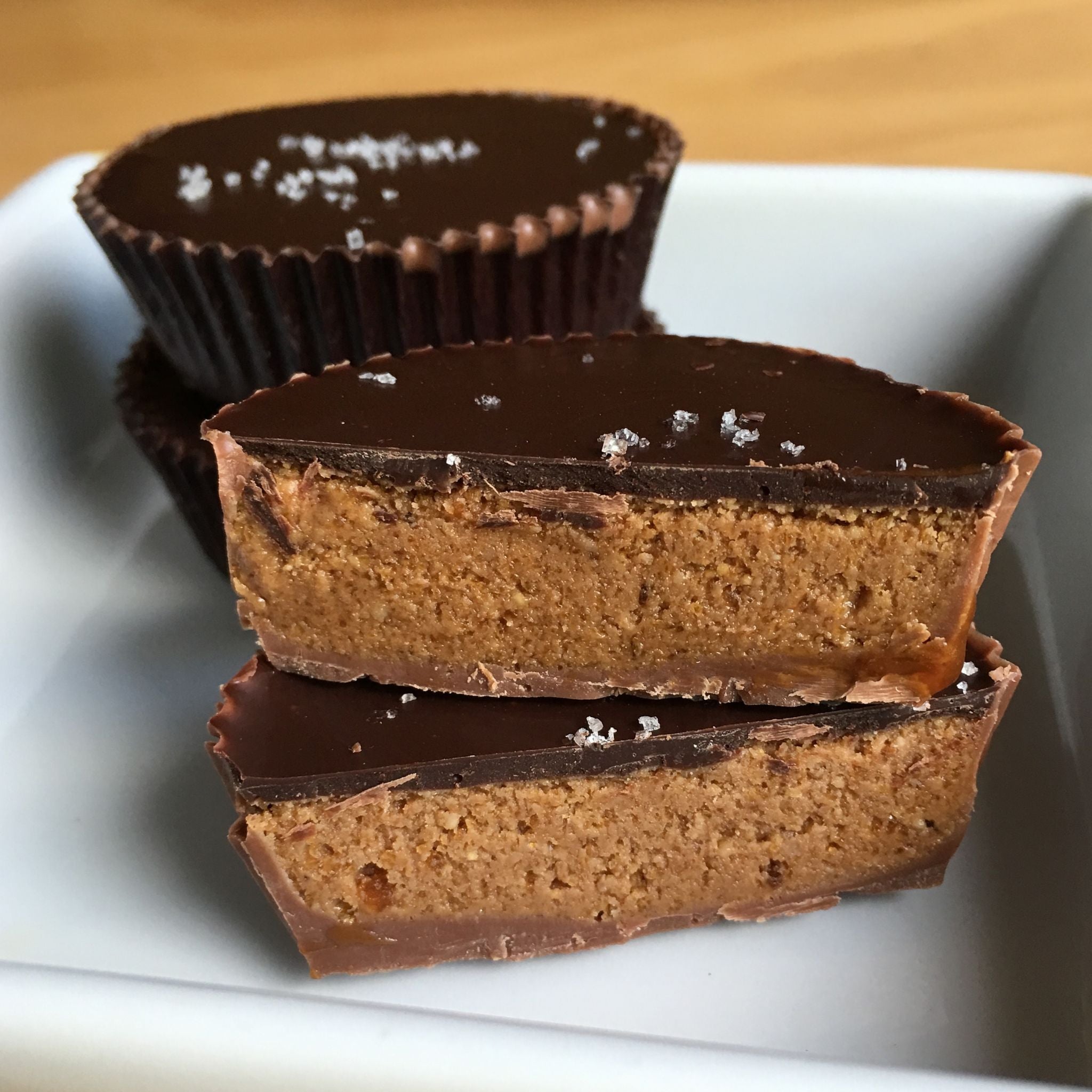 Peanut butter cup cut in half with insides showing, stack of 2 cups sitting in background, all in a white square dish.