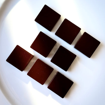 Eight square pieces of dark chocolate on a white plate