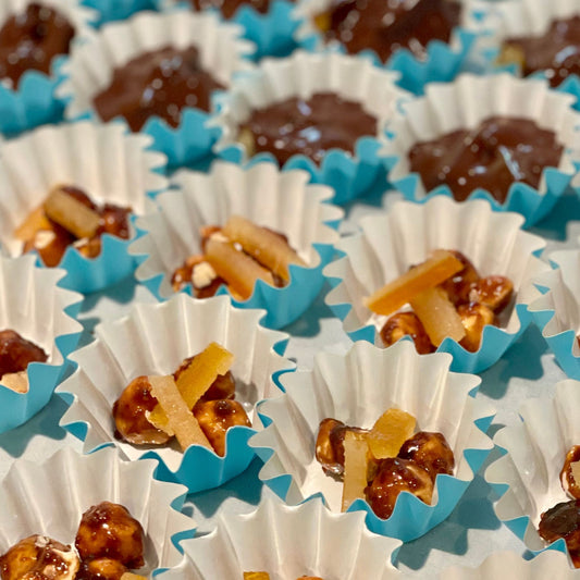 bright blue scalloped candy cups, all in a grid close together, half filled with candied hazelnuts and candied orange peel, half covered in chocolate.