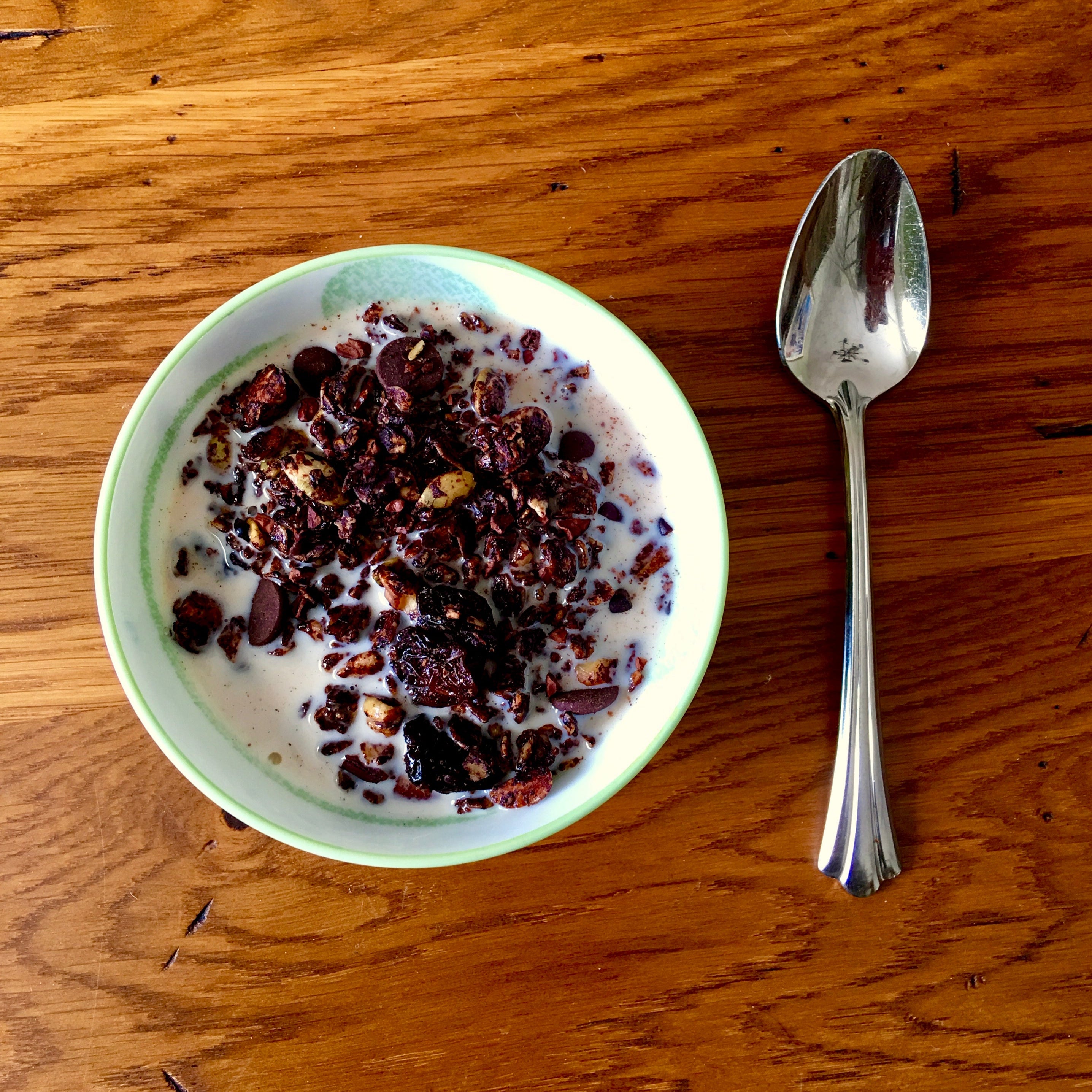Bowl of chocolate granola with milk on a wood table, spoon to the side