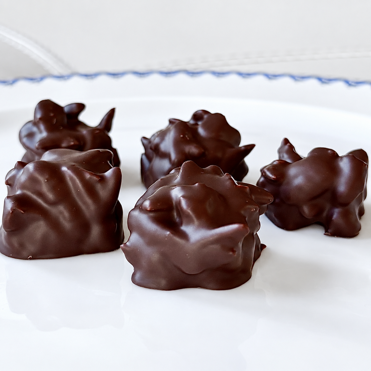 5 chocolate covered nut bunches on white plate with blue border