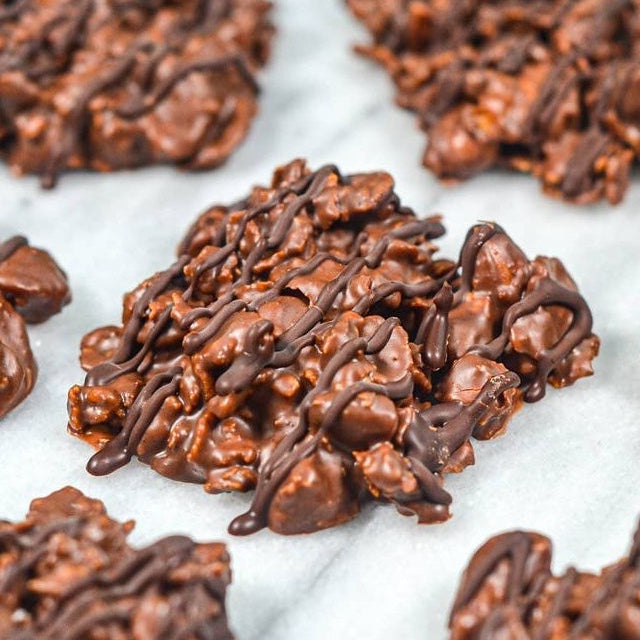 Chocolate rice krispie clusters with a drizzle of chocolate syrup, arranged on a white marble surface.