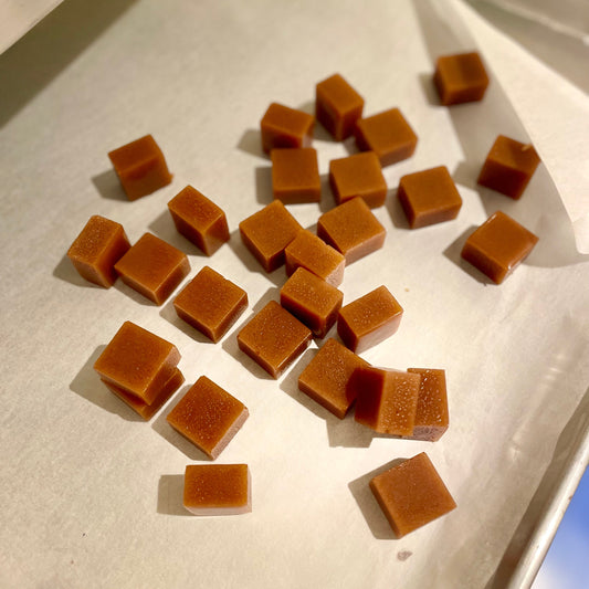 Small square-shaped brown caramels on a white tray