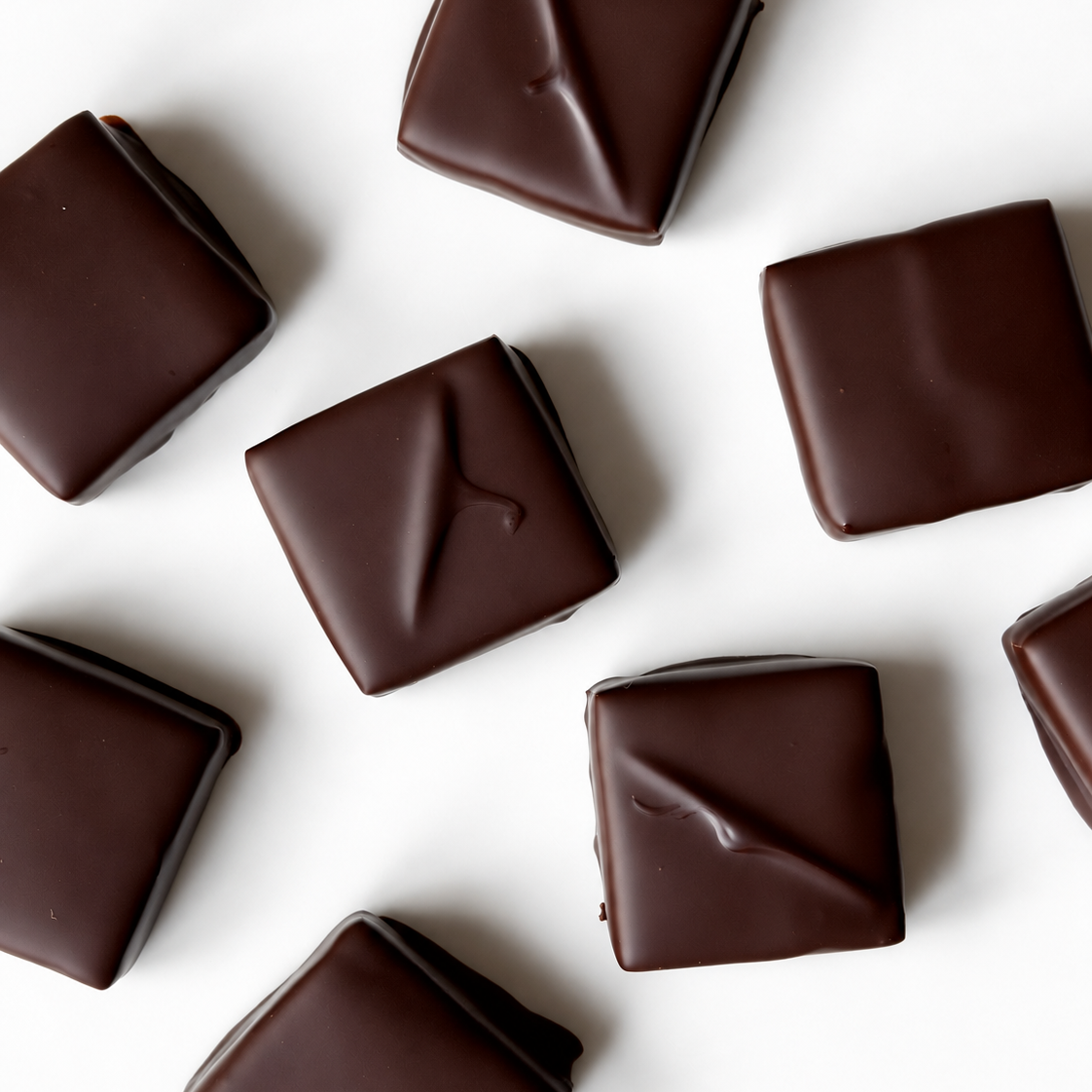 Several square pieces of dark chocolate with a glossy finish, scattered on a plain white background.