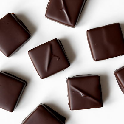 Several square pieces of dark chocolate with a glossy finish, scattered on a plain white background.