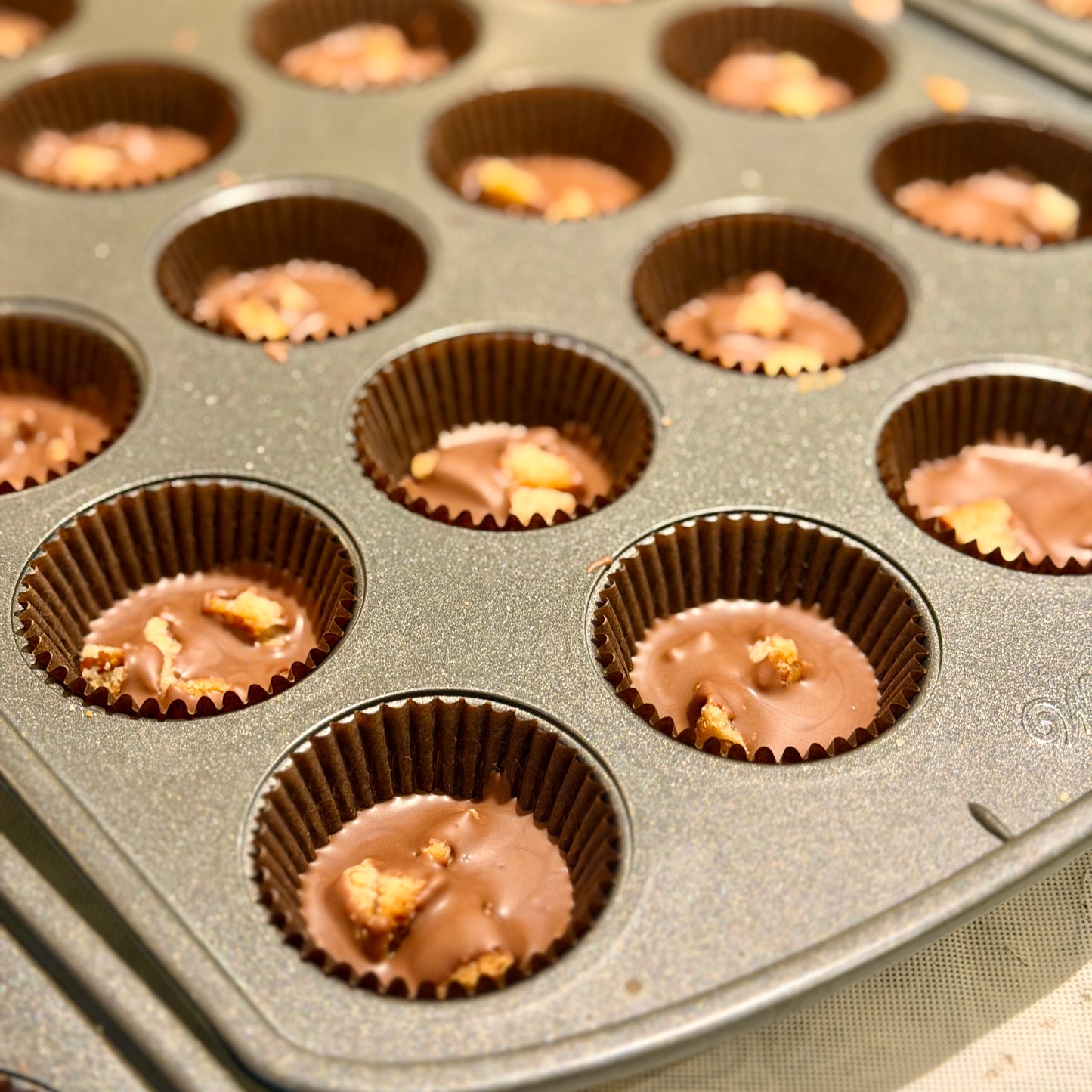 Mini muffin tin filled with chocolate and chopped cookies