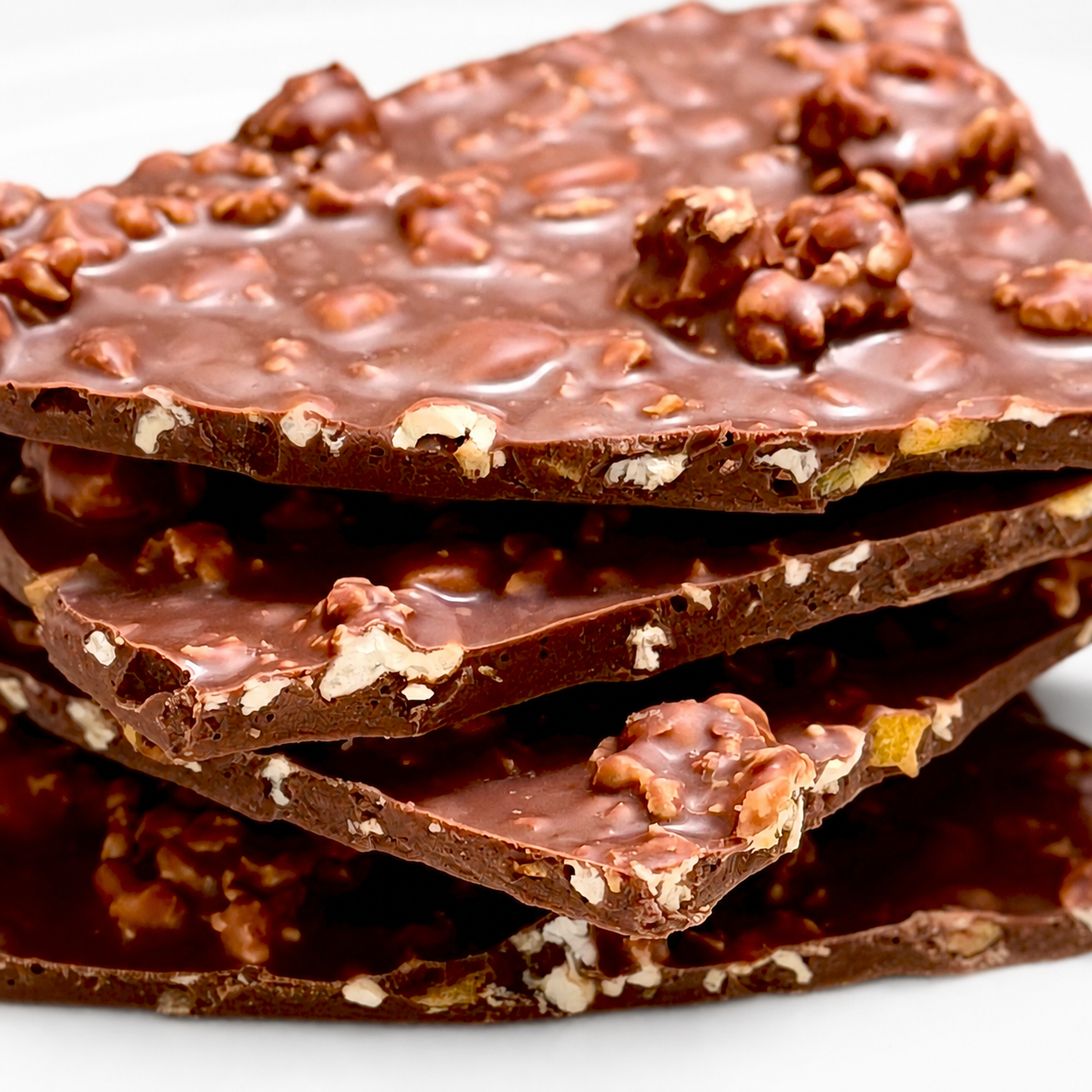 A close-up stack of thick chocolate bark with chopped nuts and white chocolate pieces on a white background.