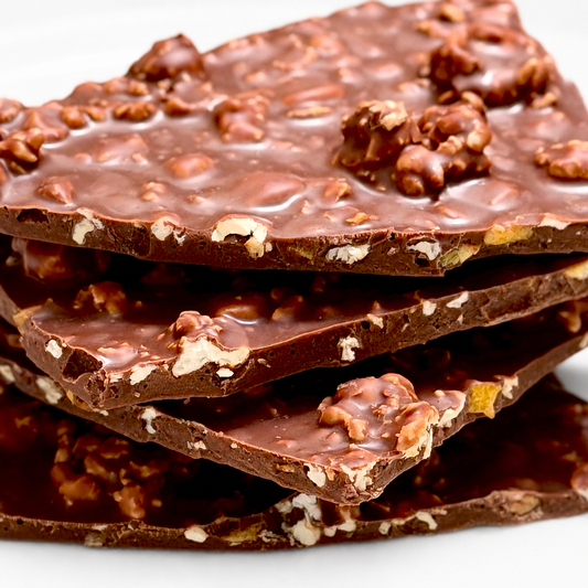 A close-up stack of thick chocolate bark with chopped nuts and white chocolate pieces on a white background.