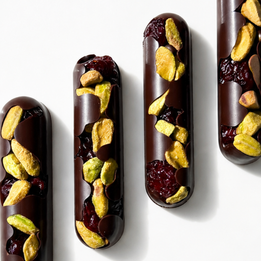 4 oblong dark chocolate bars with pistachios and tart cherrie on white background
