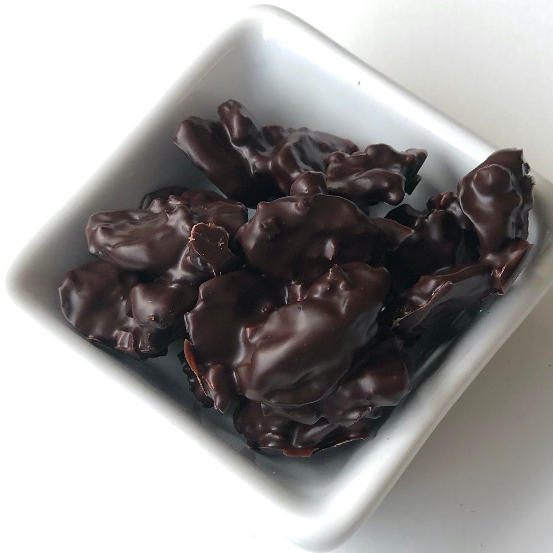 Dark chocolate covered treats in a white square bowl on a white background