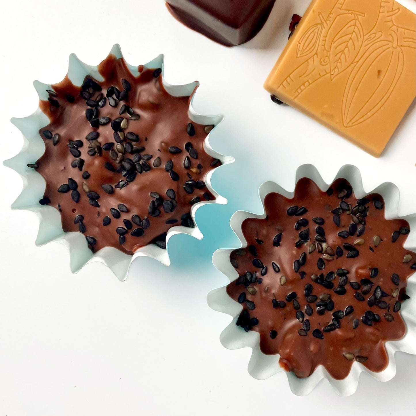 two blue candy cups filled with a dark milk chocolate with black sesame seeds sprinkled on top.