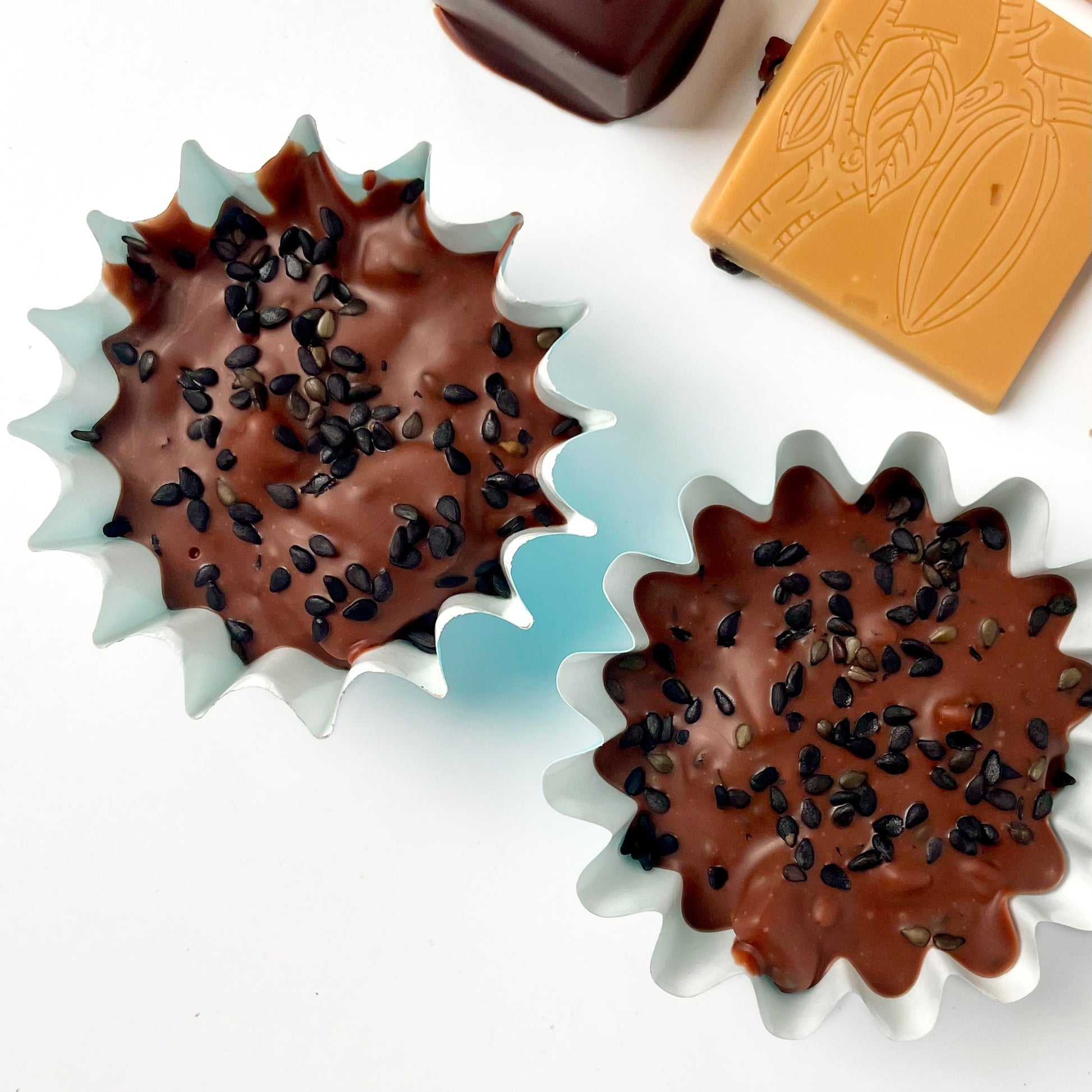 two blue candy cups filled with a dark milk chocolate with black sesame seeds sprinkled on top.