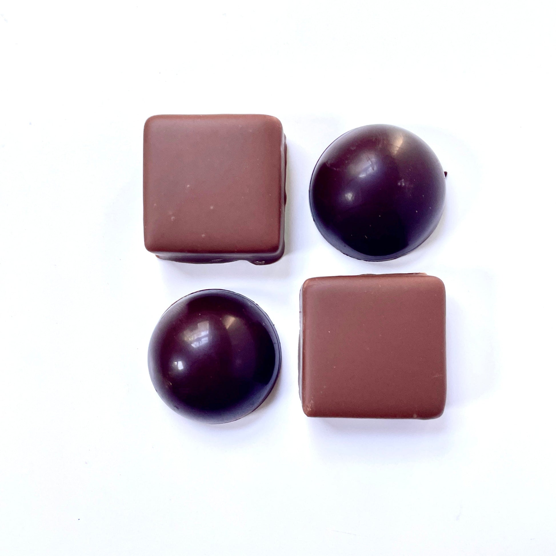 Four chocolate candies, two square and two round, on a white background