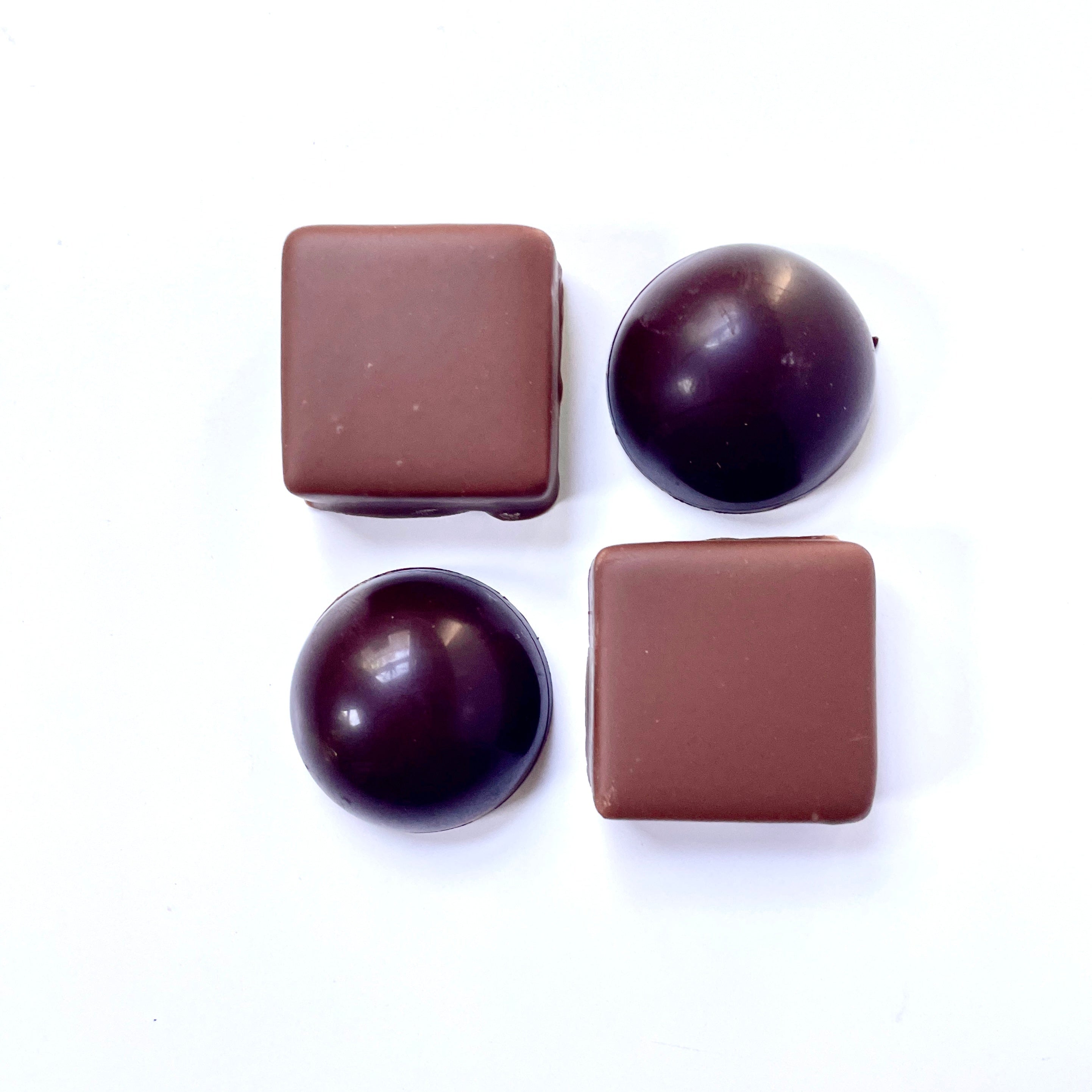 Four chocolate candies, two square and two round, on a white background
