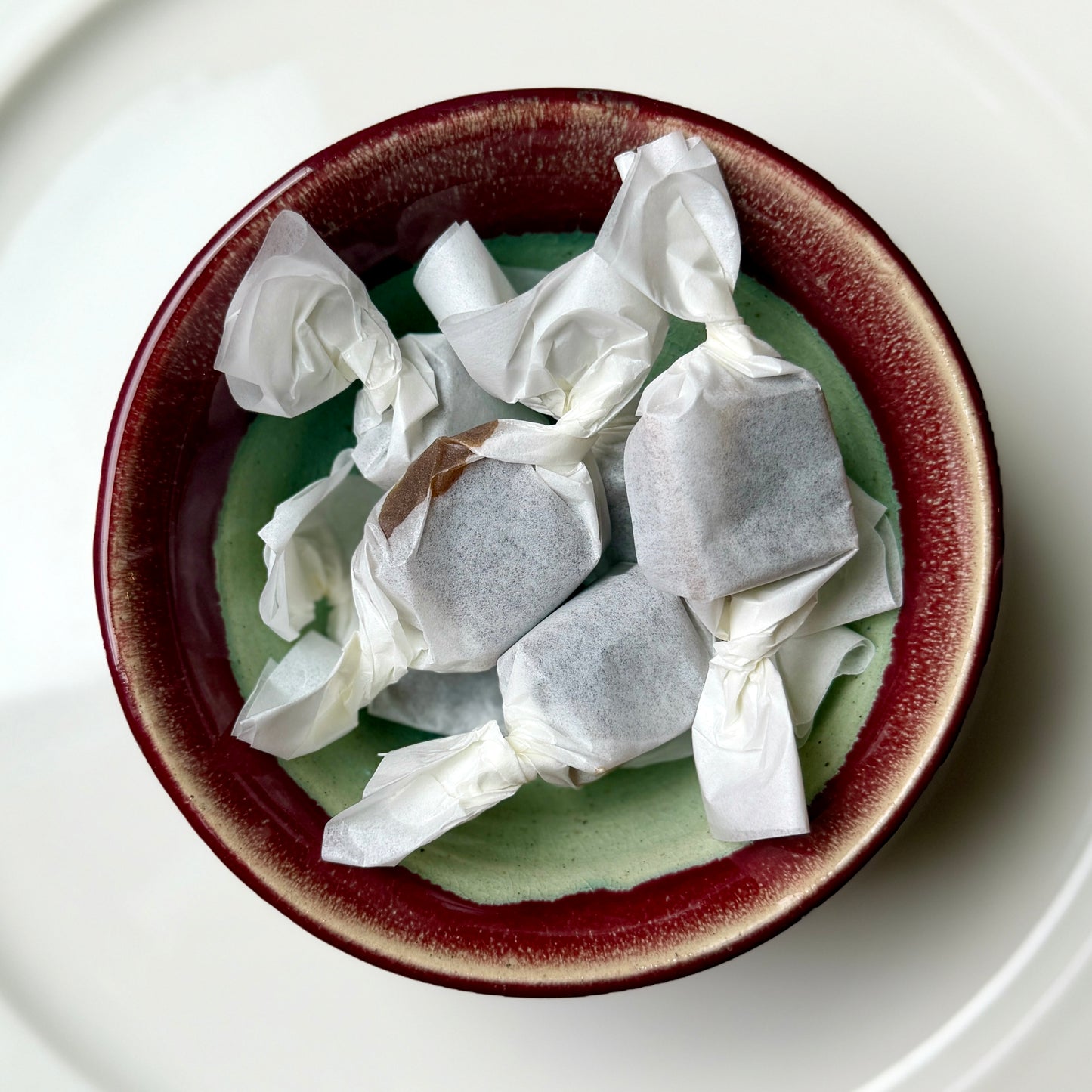 Candies wrapped in white paper inside a brown bowl on a white plate