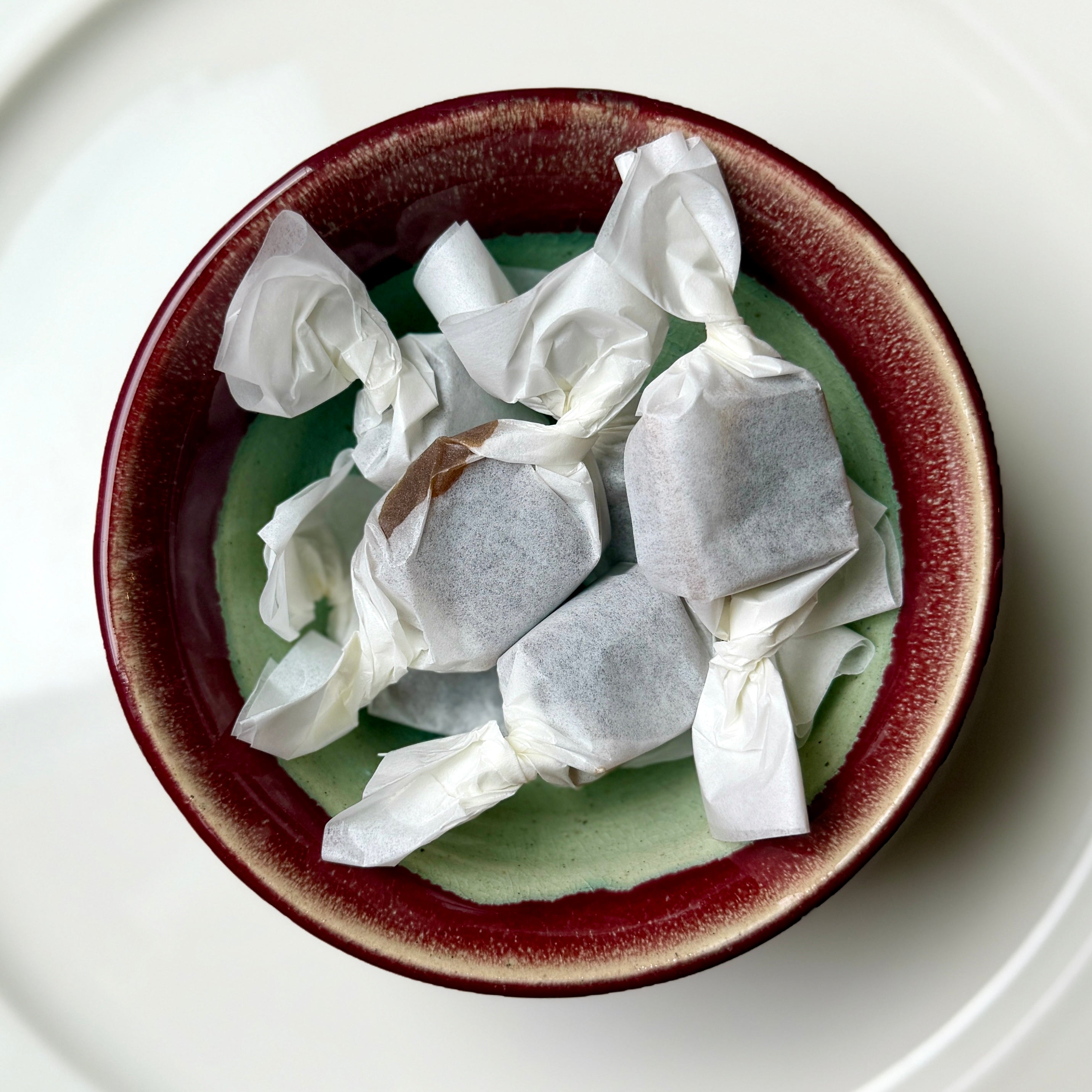 Candies wrapped in white paper inside a brown bowl on a white plate