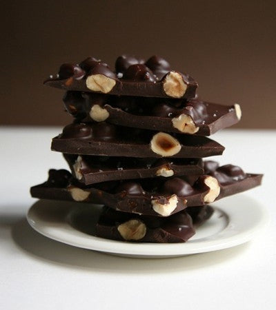Stack of dark chocolate bars with nuts on a white plate against a brown background