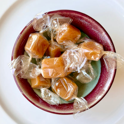 Caramel candies in clear wrappers inside a ceramic bowl on a white background