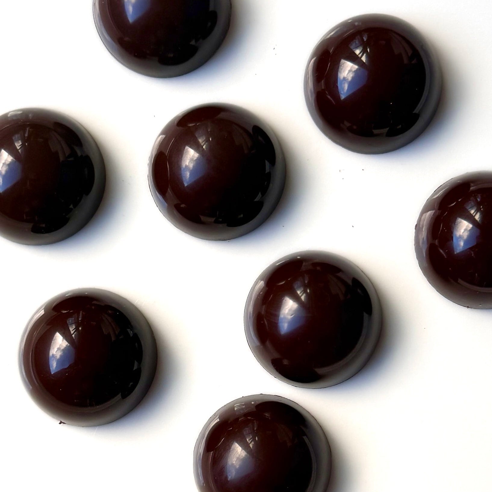 eight dark brown half dome chocolates on a white background